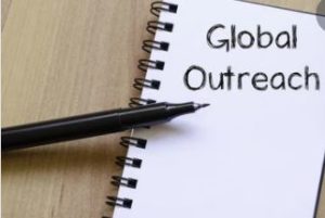 Image contains a pen and a notebook with a handwritten note, saying Global Outreach