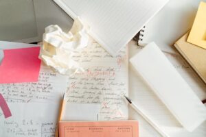 Desk cluttered with notebooks, crumpled paper, and handwritten notes marked with red edits, representing content marketing tools in action.